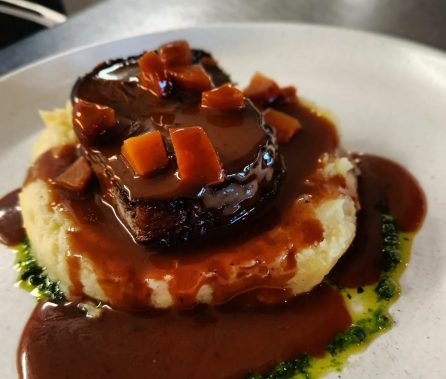 Plat de viande sur purée avec sauce brune et garnitures de légumes.