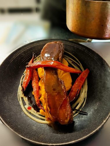 Plat de viande avec sauce, carottes rôties et purée sur assiette noire.